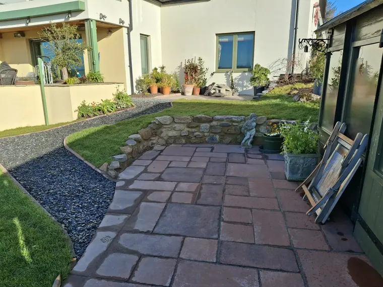 A paved terrace tucked into the corner of the house, with a slate mulch strip separating lawn from paving.