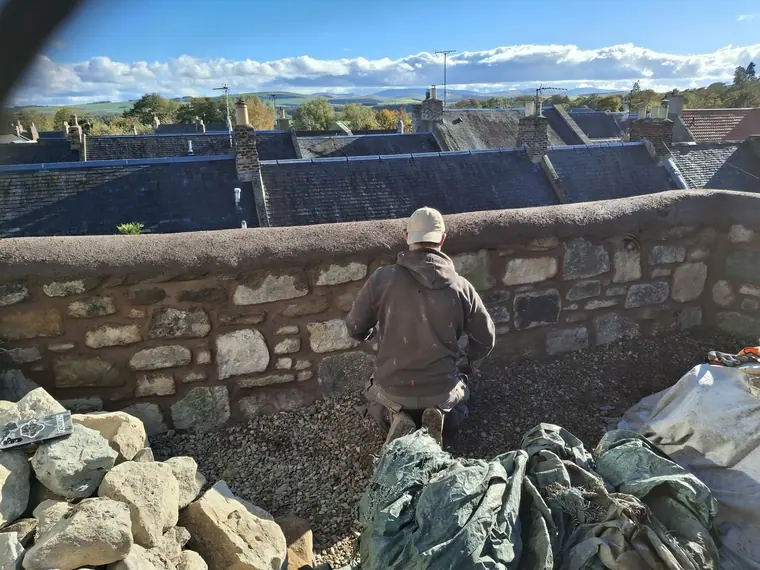 Rebuilding a boundary wall above the rooftops, sorting stone by size before it goes back on the wall.