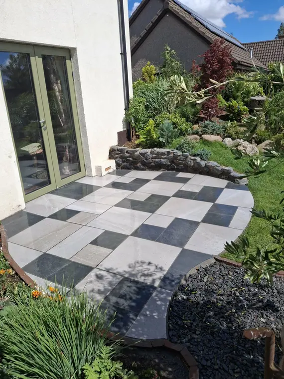 A chequerboard porcelain patio with a curved stone retaining edge — square pattern, curved boundary, no cut left ragged.