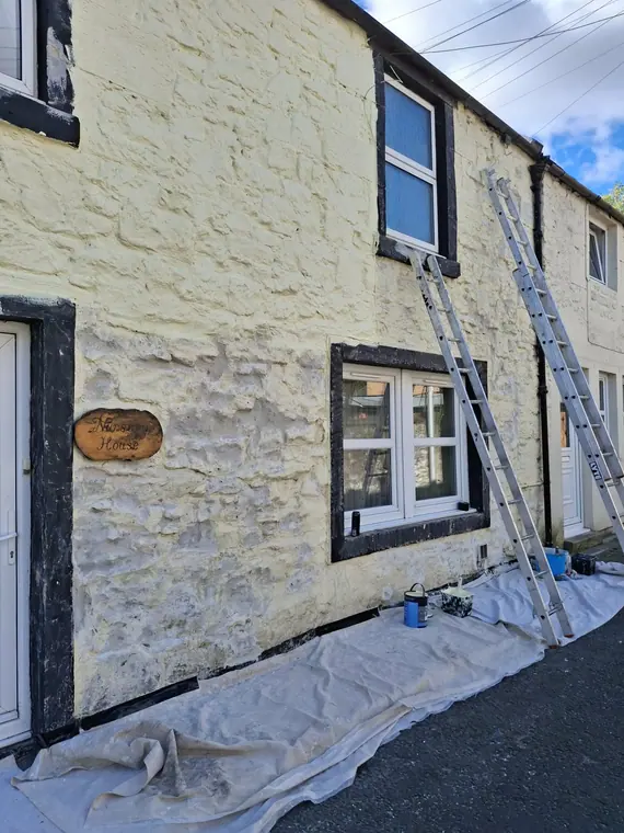Ladders and dust sheets out on a terraced cottage, patching the render before the topcoats go on.