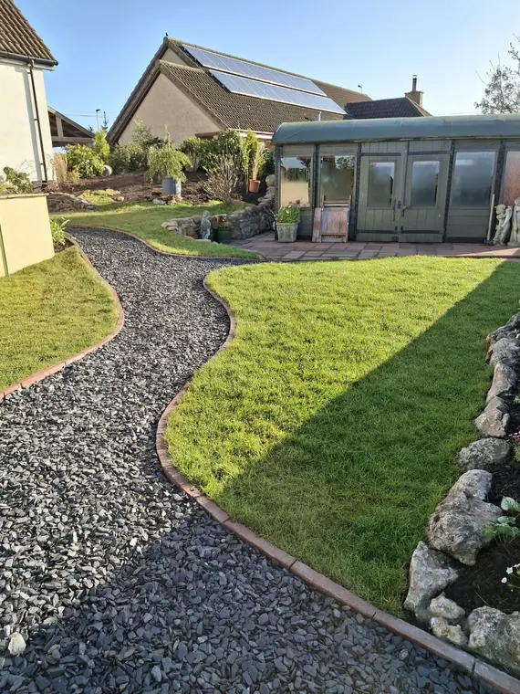 A sweeping gravel path cutting between lawn and boulder border, edged so it will not spill.