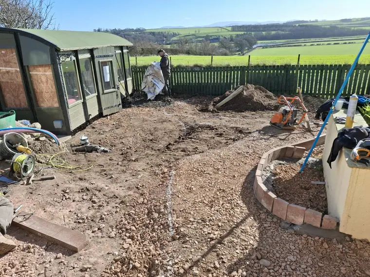 Groundwork under way with the field behind — sub-base first, every time, on ground that holds water.