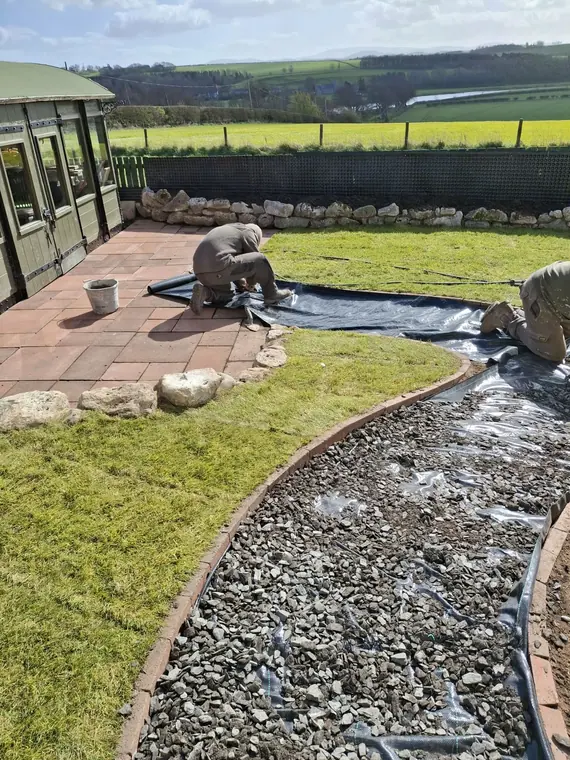Weed membrane lapped and pinned under the gravel run — the part nobody sees that decides how it ages.