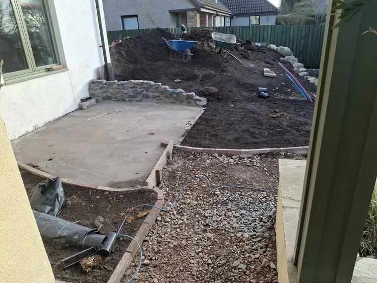 A stone retaining wall built to hold the upper level, with the base slab already down beside it.
