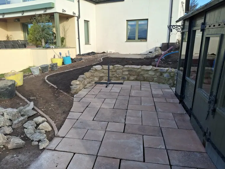 Riven sandstone paving laid tight to a new stone retaining wall, with the bed line following the house.