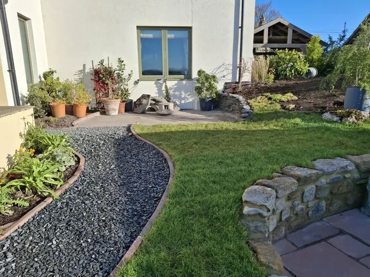 Slate mulch border curving around a new lawn, with a stone retaining wall holding the level behind.