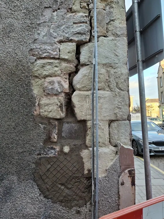 Severely spalled quoins on a corner shopfront, with cement repairs already failing and the stone crumbling behind.