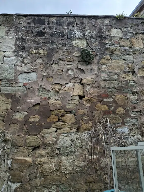 A badly eroded street wall with washed-out joints and loose face stones, surveyed before quoting.