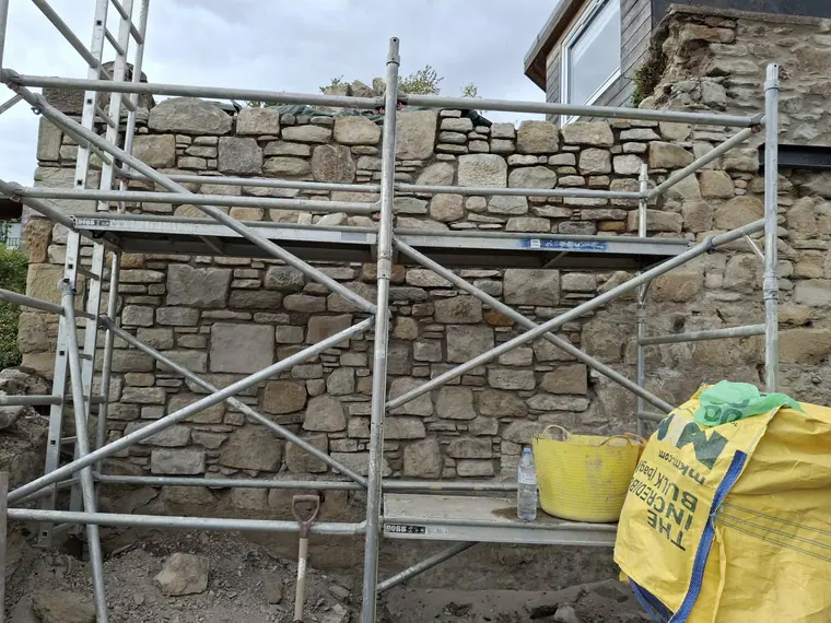 Pointing a mixed sandstone and whinstone wall from a scaffold, working top down to keep the face clean.