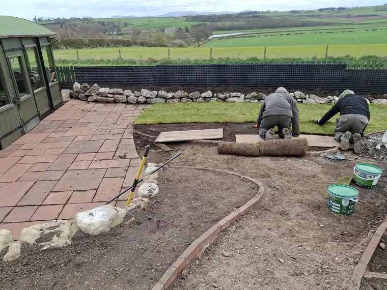 Turf and paving landing together at the end of a build, with the field boundary tidied behind.