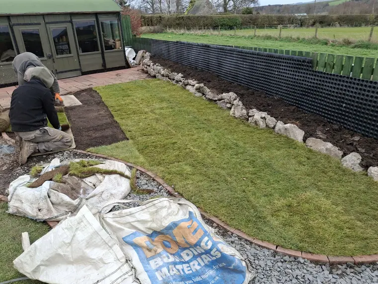 Fresh turf going down against a boulder border, cut to the curve rather than forced to fit.