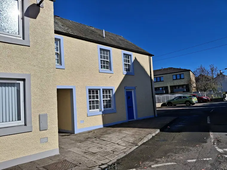 Same house from the corner, the render repaired and repainted so the wall reads as one clean plane.